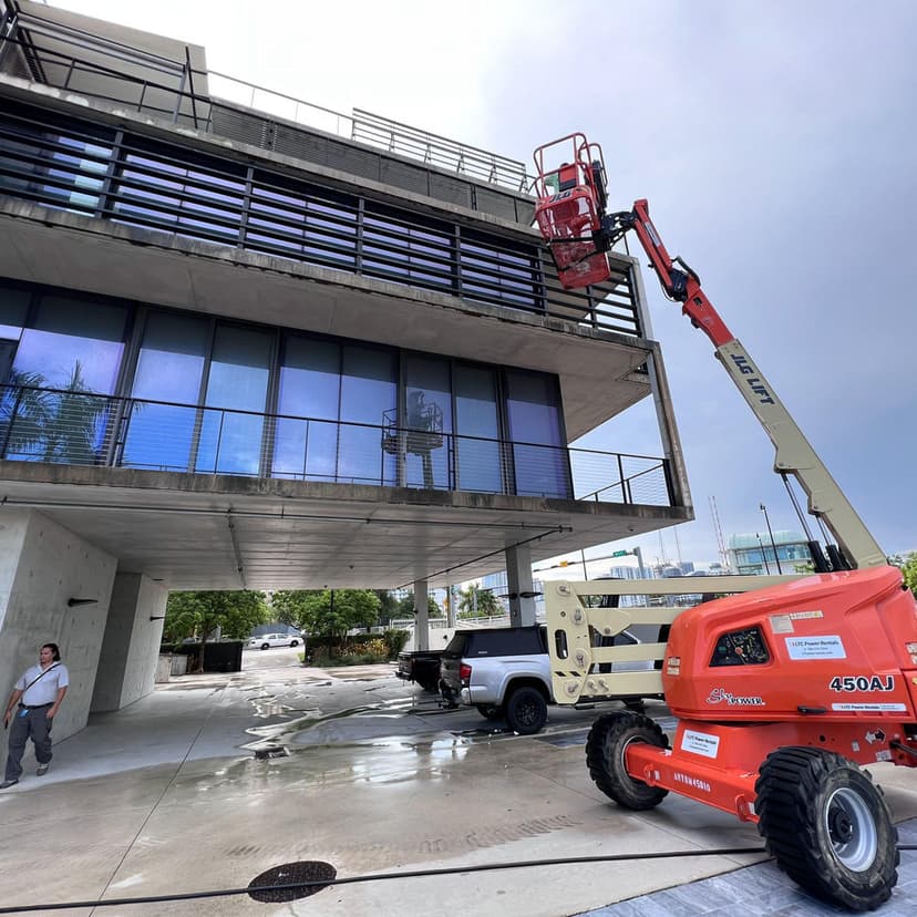 Construction worker using a cherry picker lift on a building's exterior with cloudy sky background.
