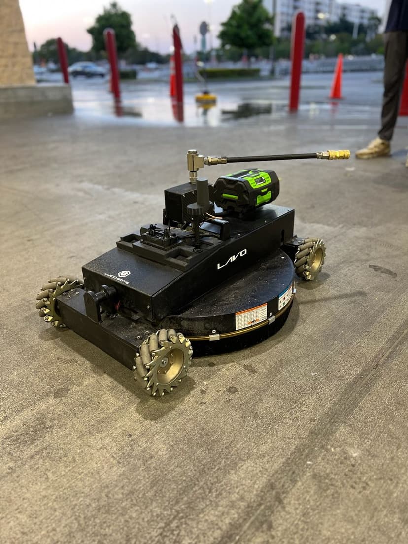 Autonomous cleaning robot with wheels and spray attachment in a parking lot setting.