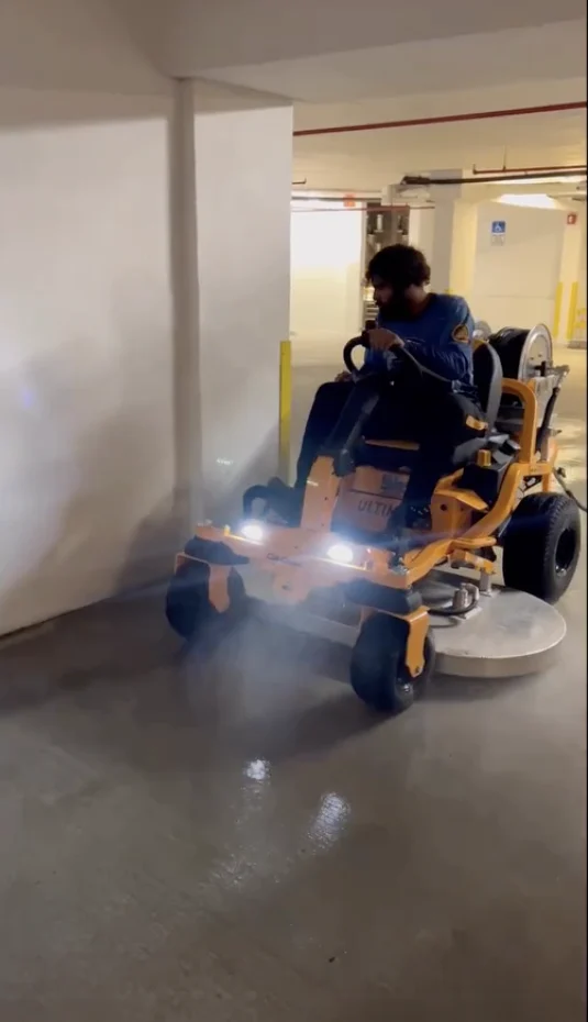 Pressure Kleen operator using a custom ride-on machine with surface-cleaning attachments inside a parking garage